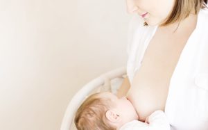 Neugeborenes wird von Mom-to-Be gestillt, mit sichtbarem Babykopf und Mutterbrust